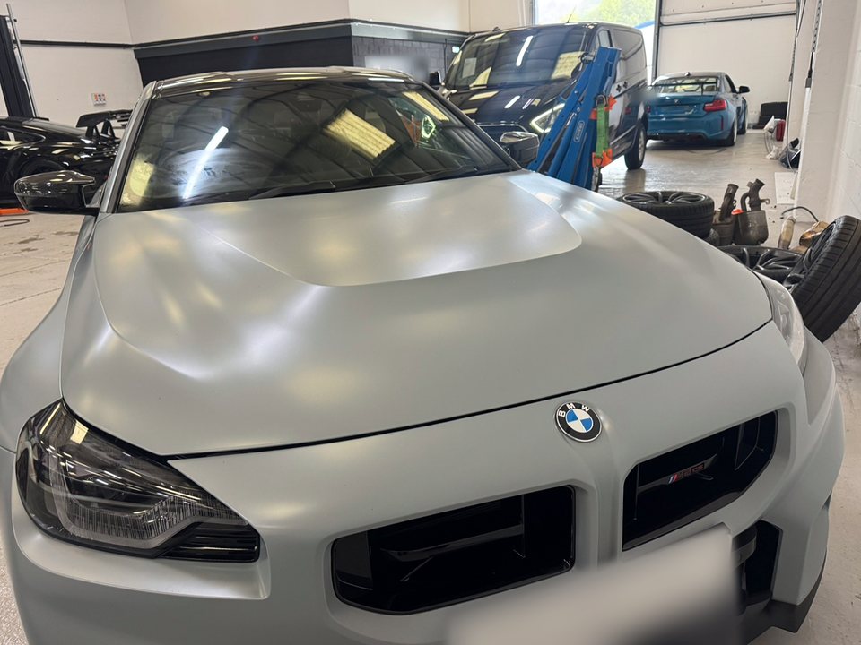 Matte grey BMW M2 with a fitted windscreen, parked inside a motor trade workshop, number plate blurred
