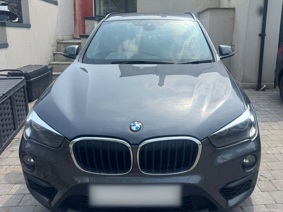 Grey BMW X1 with a newly fitted windscreen, parked on a driveway, number plate blurred